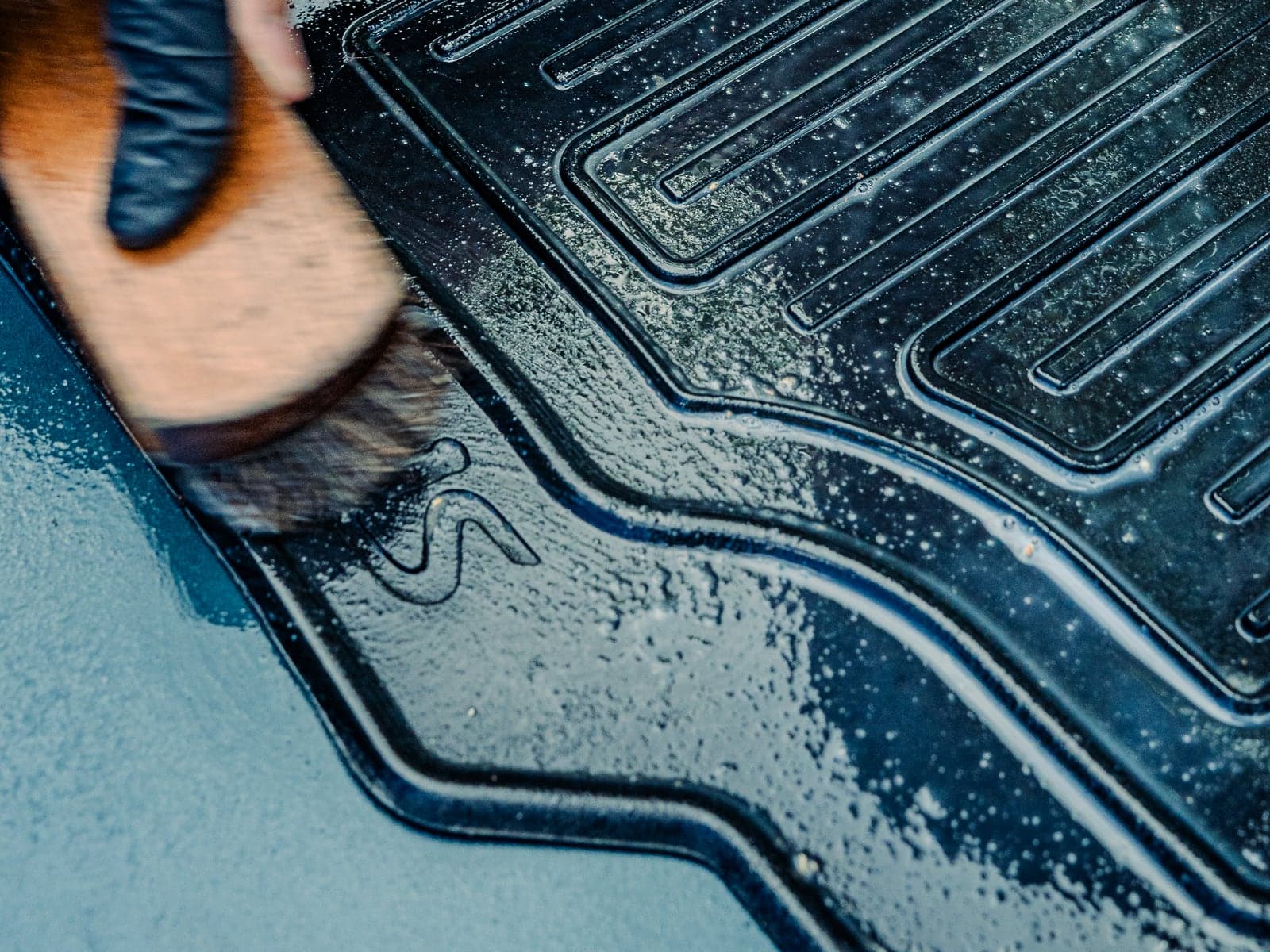 Brossage énergique d'un tapis sorti du véhicule, pour décoller la terre incrustée dans la trame