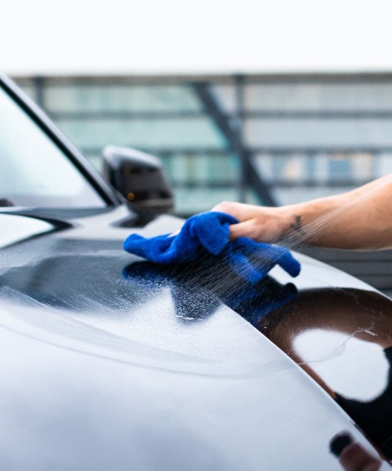 Nettoyage de la carrosserie d'une voiture noire au spray et à la microfibre, sans eau
