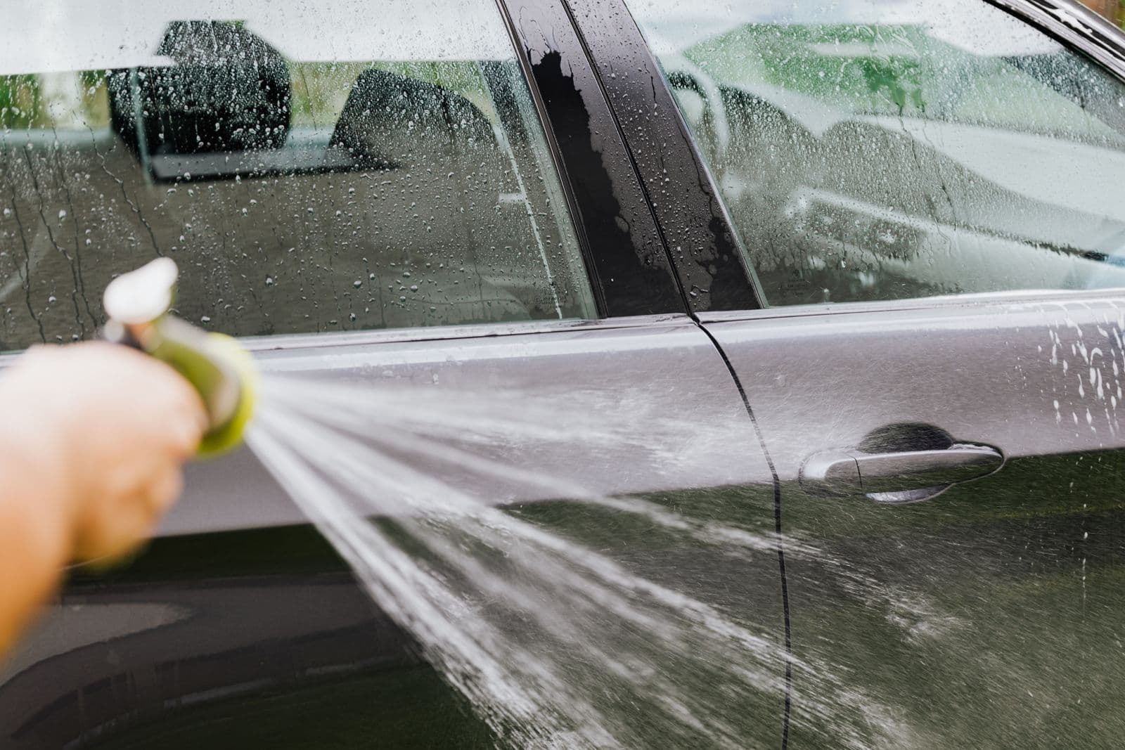 Jet d'eau projeté sur la carrosserie d'une voiture lors d'un lavage traditionnel